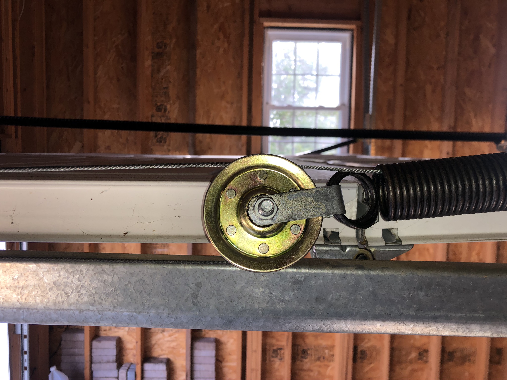 Brass cable pulley with steel bracket beside an extension spring on a galvanized track